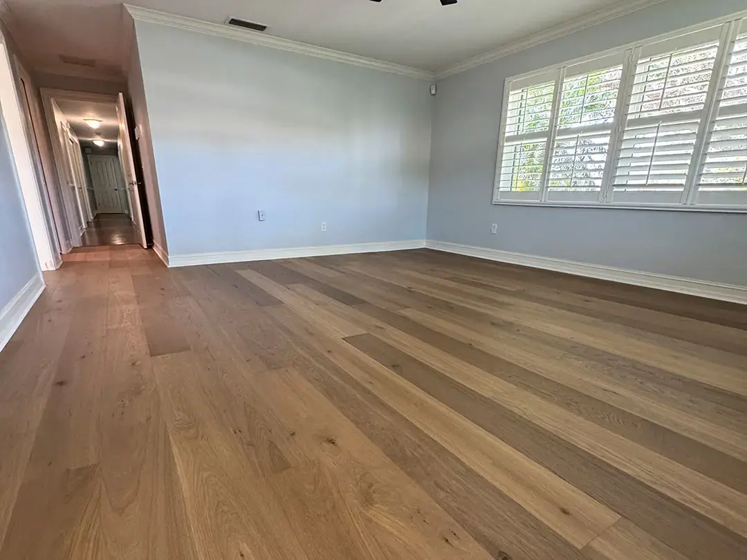 How Did Engineered Wood Floor Installation Transform This Dunedin, FL Home? Empty room with newly installed light-colored engineered hardwood flooring, pale blue walls, white baseboards, and a large wi