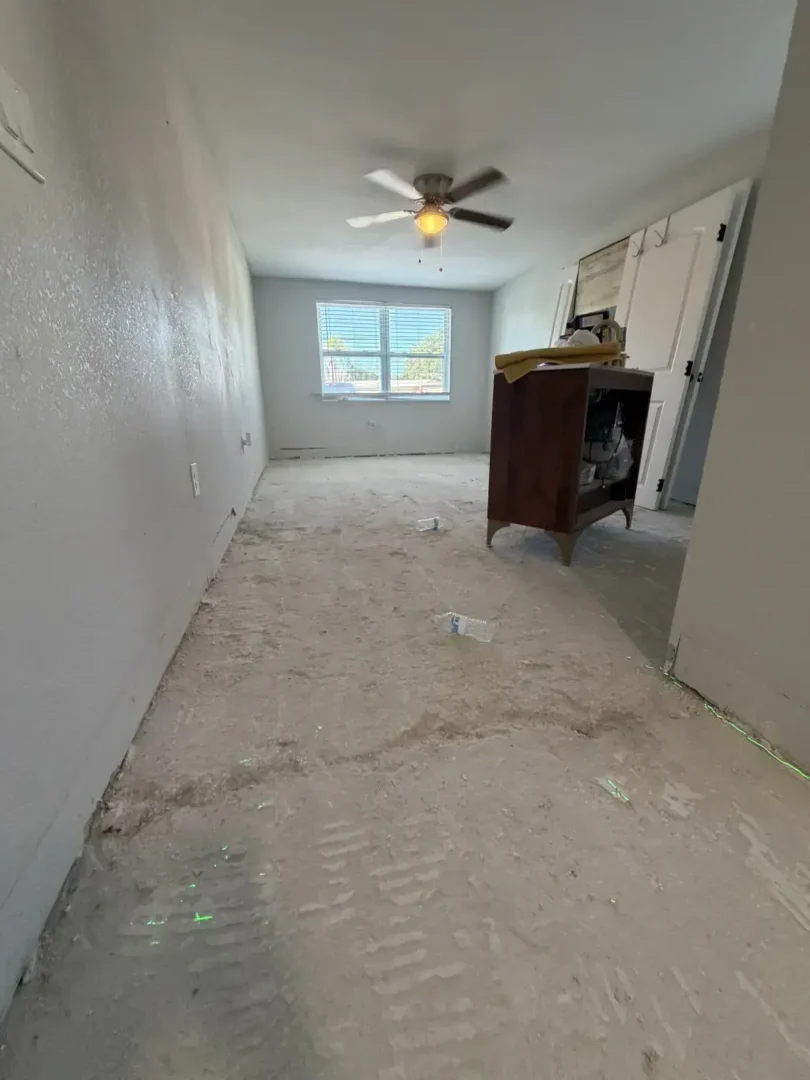 Empty room with concrete floor under renovation, white walls, ceiling fan, and window with blinds in natural light