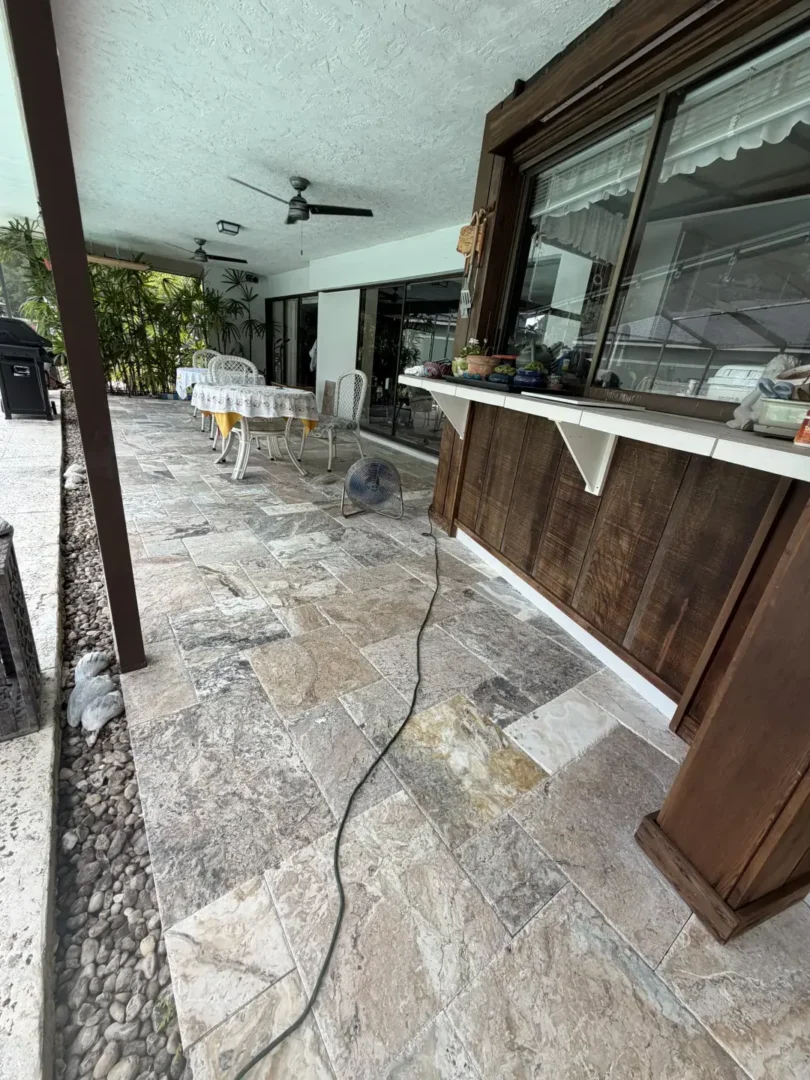 Stone tiled patio with outdoor furniture, plants, and wooden bar under covered area near pool