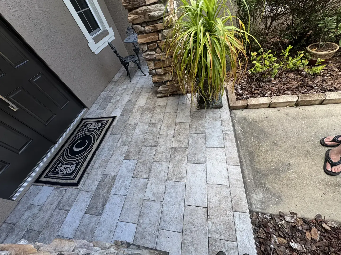 How Did Our Tile Floor Installation Transform This Front Entry in Odessa, FL? Porcelain tile floor installed on a residential front entryway in Odessa, FL with stone columns and landscaping
