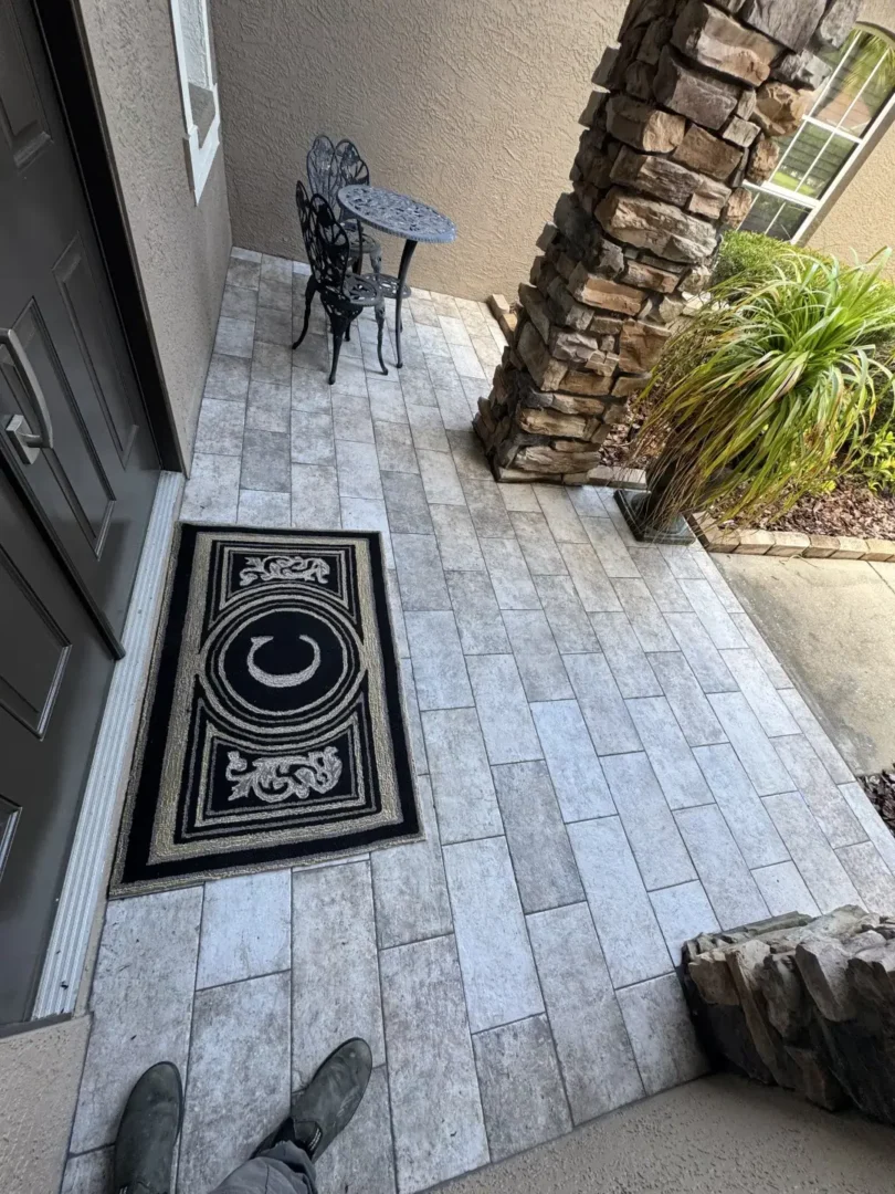 How Did Our Tile Floor Installation Transform This Front Entry in Odessa, FL? Porcelain tile floor installed on a residential front entryway in Odessa, FL with stone columns and landscaping