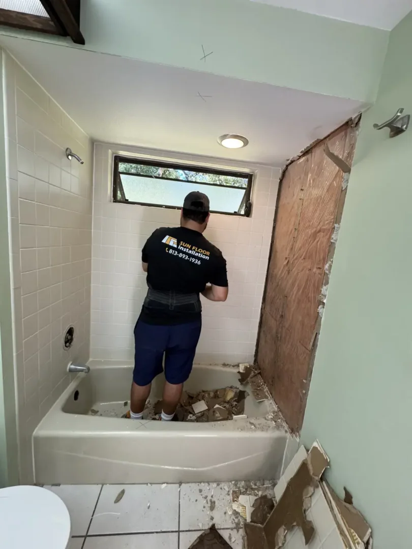 Let's Transform Your Bathroom Together Contractor removing shower wall tile during a bathroom renovation, with debris in the bathtub