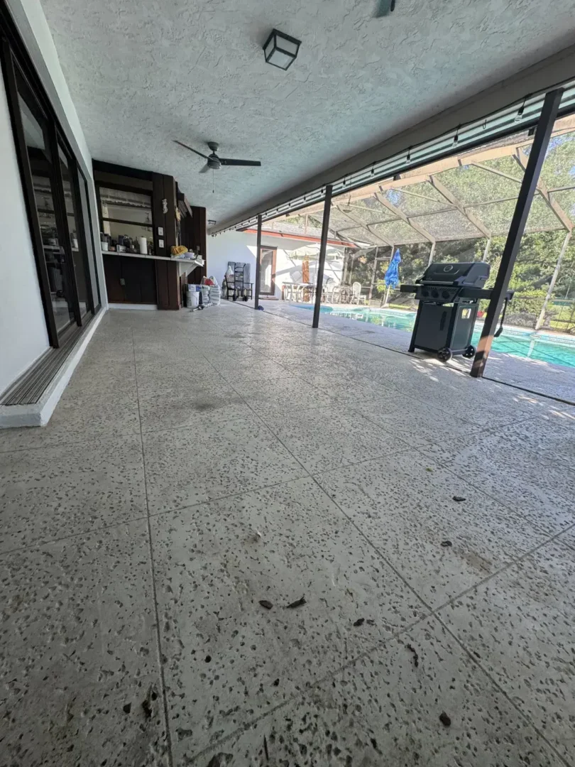 Wide view of patio with speckled tile floor, ceiling fans, and pool with black grill on patio