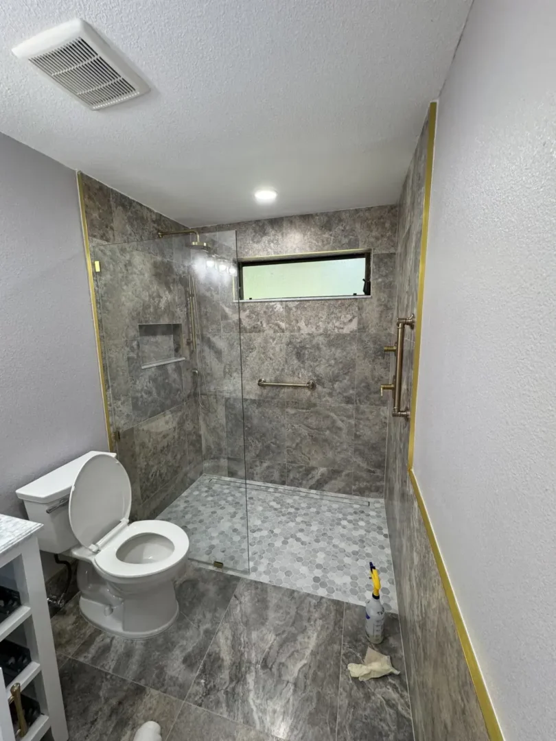 Let's Transform Your Bathroom Together Walk-in shower with gray tile, frameless glass door, and grab bars in a modern bathroom