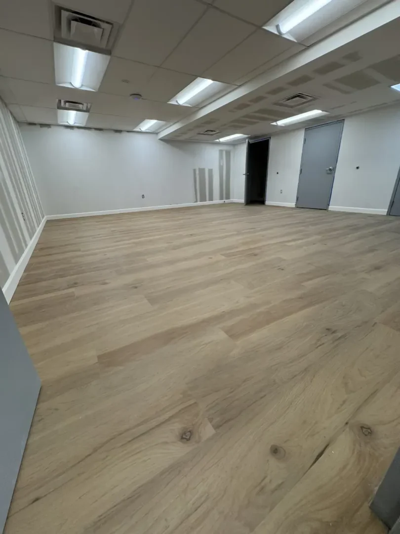 Empty commercial room with light wood-look flooring, white walls, and fluorescent ceiling lights